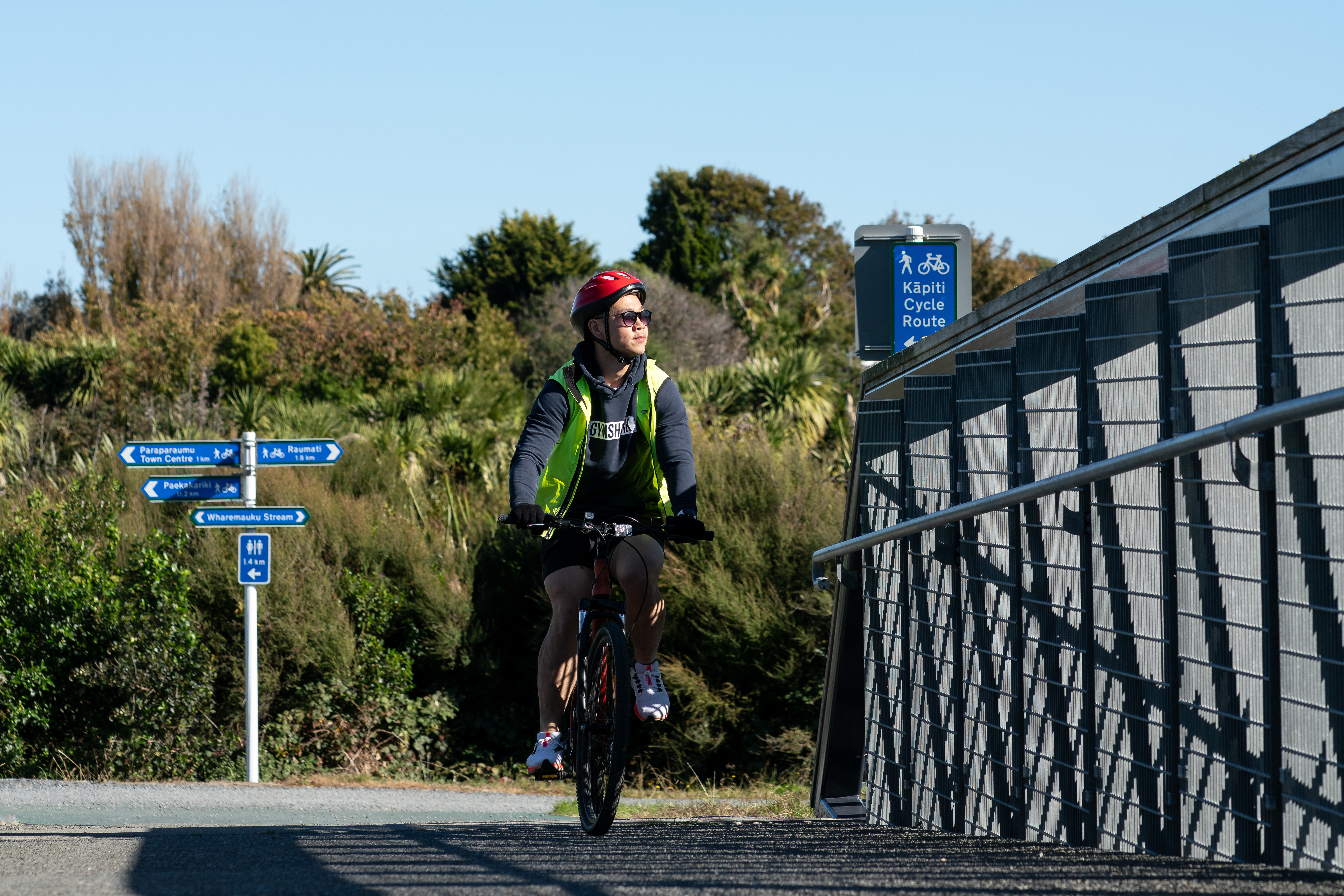 Cyclist riding over a bridge on the Kāpiti Cycle Route with signs to Paraparaumu and Raumati in the background