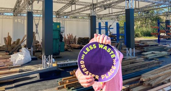 The new Zero waste hub in Otaihanga with piles of recycled wood and a man in front holding a 'Less waste, greater place' sign.