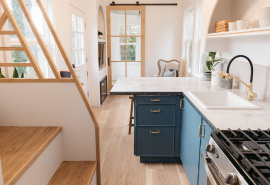 Photo of a tiny home kitchen bench, sink and gas hob, looking towards a seating area and sliding door.