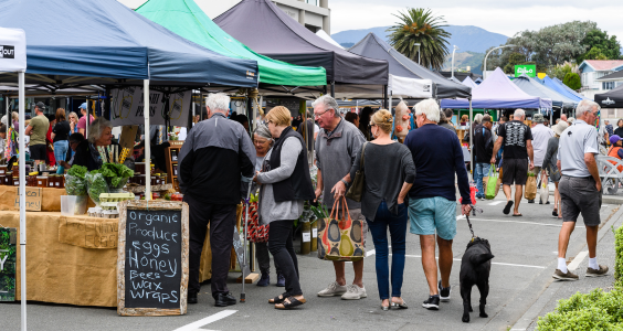 A busy day at one of our local markets – a group of people speak with a stallholder selling organic product.